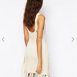 May include: A white crochet dress with a sleeveless design and a slightly flared skirt. The dress has a delicate, open-weave pattern and a slightly shorter hemline in the front.