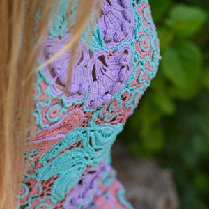May include: A close-up of a crocheted top with a delicate floral pattern in shades of pink, blue, and purple.