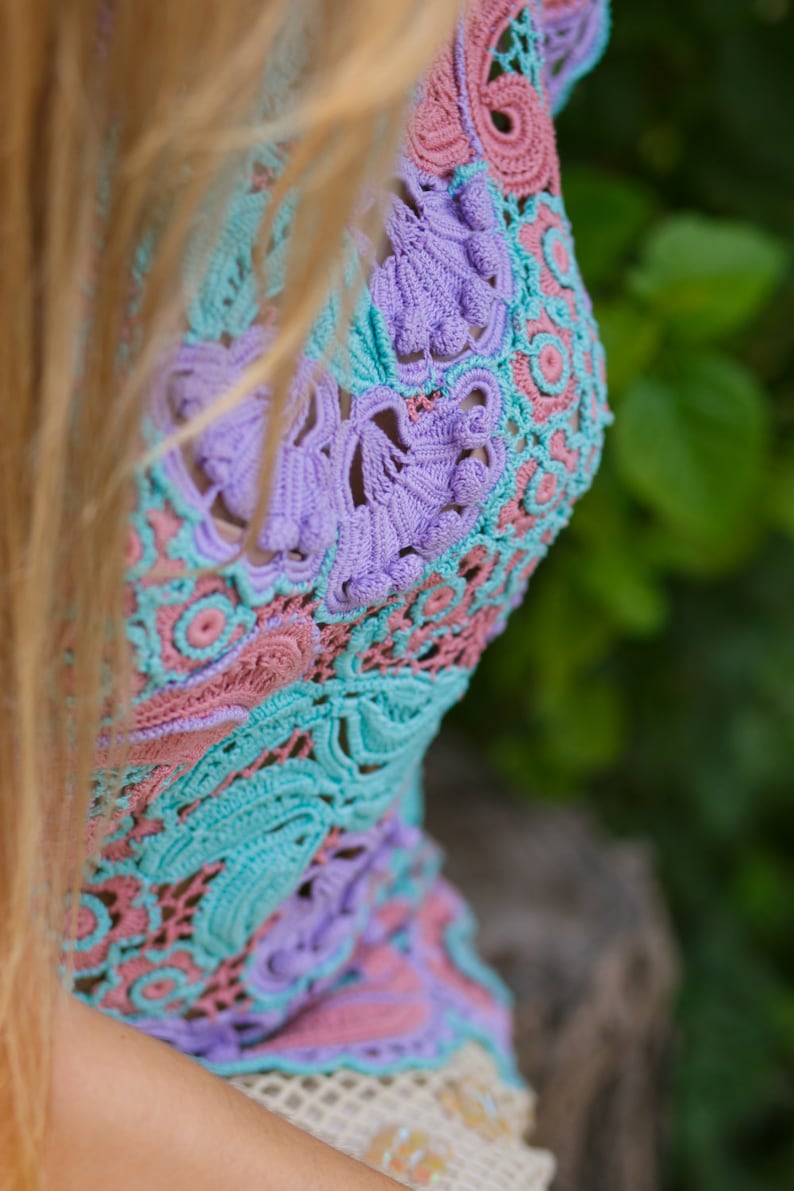 May include: A close-up of a crocheted top with a delicate floral pattern in shades of pink, blue, and purple.
