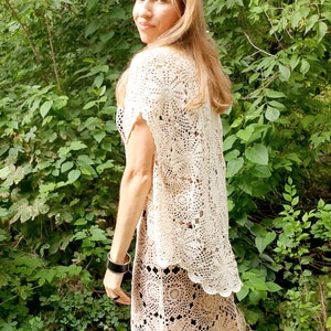 May include: A white crochet top with a scalloped hemline. The top is made with a delicate openwork pattern and has short sleeves.