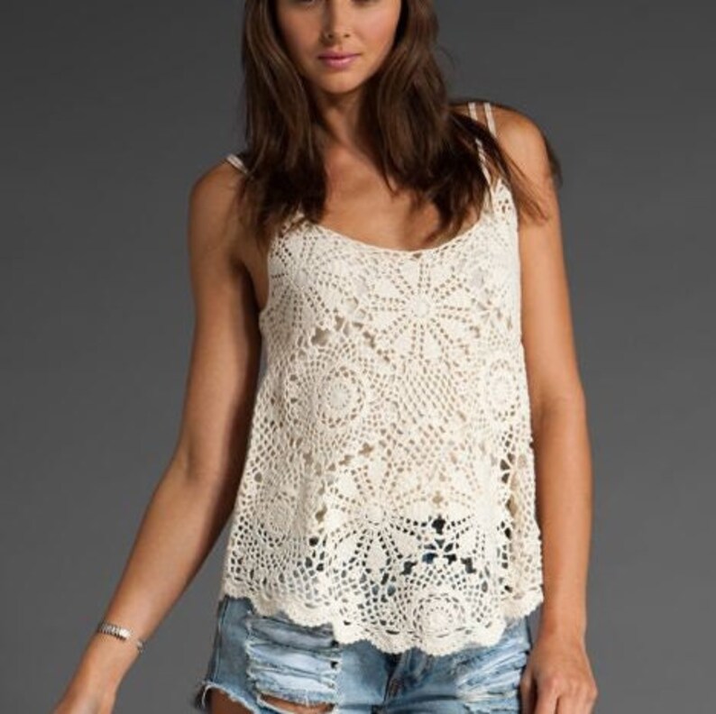 May include: A white crochet tank top with a delicate floral pattern. The top has a loose fit and a scalloped hem.