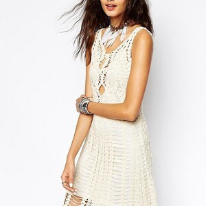 May include: A white crochet dress with a loose fit and a scalloped hem. The dress has a scoop neck and a sleeveless design.