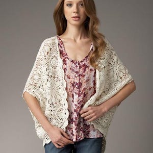 May include: A white crocheted cardigan with a floral print blouse underneath. The cardigan has a delicate lace pattern and a loose fit.