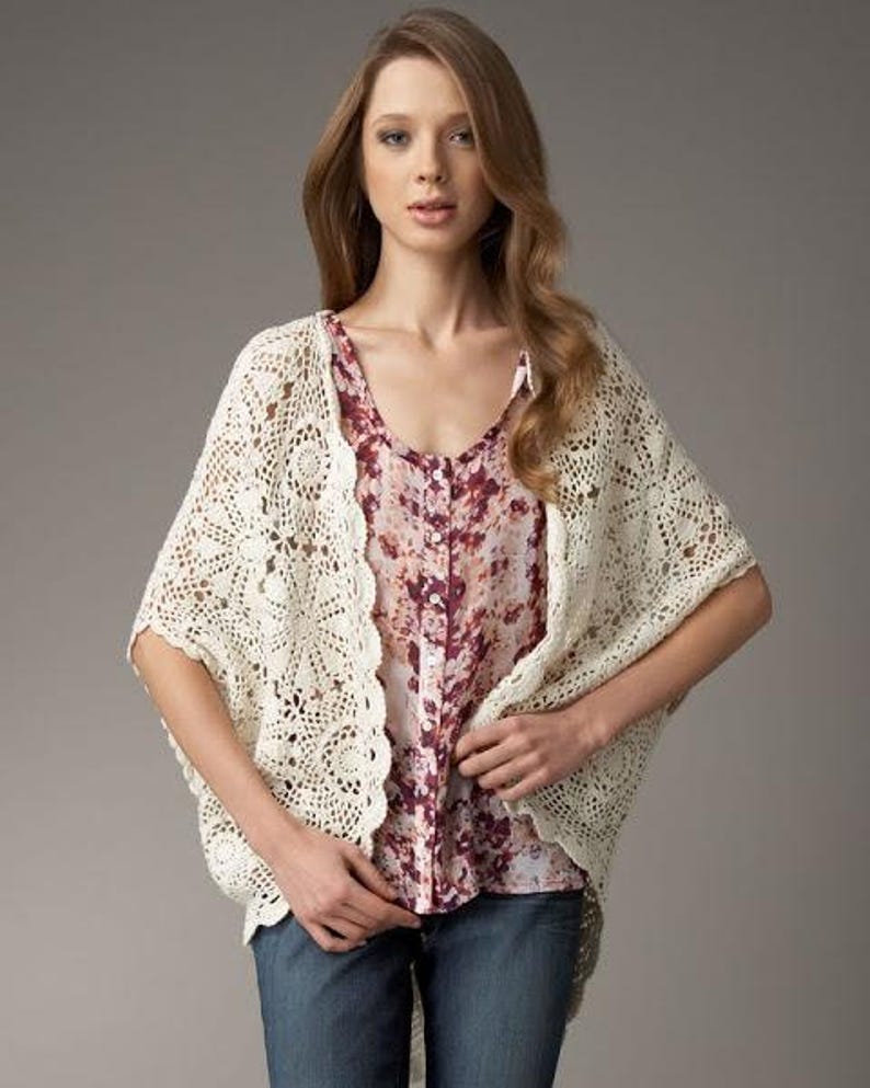 May include: A white crocheted cardigan with a floral print blouse underneath. The cardigan has a delicate lace pattern and a loose fit.