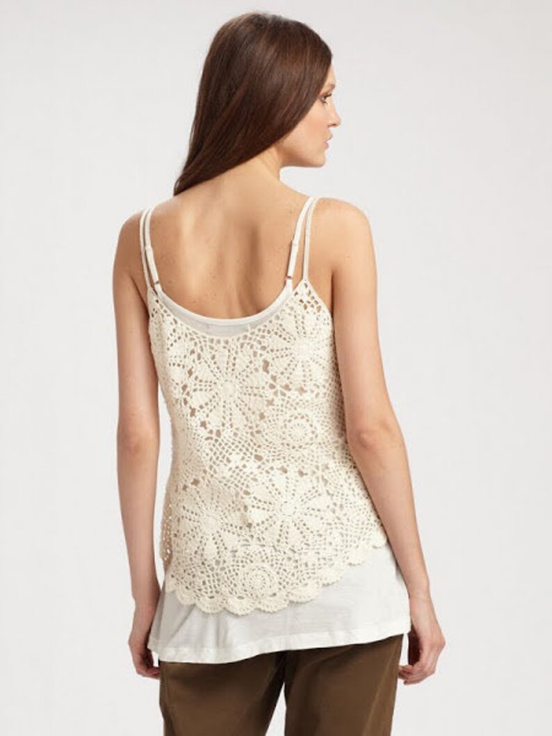 May include: A white crochet tank top with a layered look. The top has a delicate crochet pattern and a relaxed fit.
