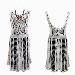 May include: A white crochet dress with a sleeveless design and a scalloped hem. The dress is shown on a white mannequin.