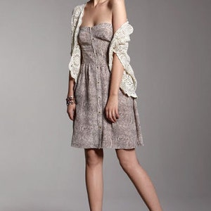 May include: A woman wearing a white crochet cardigan over a brown and white patterned dress. She is wearing brown heeled shoes.