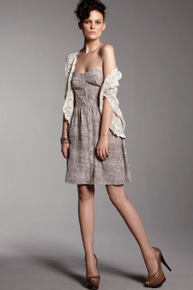 May include: A woman wearing a white crochet cardigan over a brown and white patterned dress. She is wearing brown heeled shoes.