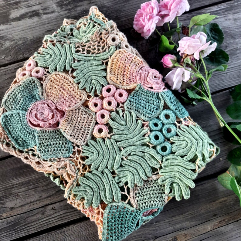 May include: A crocheted pillow with a floral design in shades of green, pink, and beige. The pillow is made with intricate stitches and has a delicate, feminine feel.