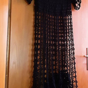 Puede incluir: Un vestido maxi de crochet negro con cuello redondo y mangas cortas. El vestido est&aacute; hecho de una tela ligera y aireada y tiene una silueta fluida.