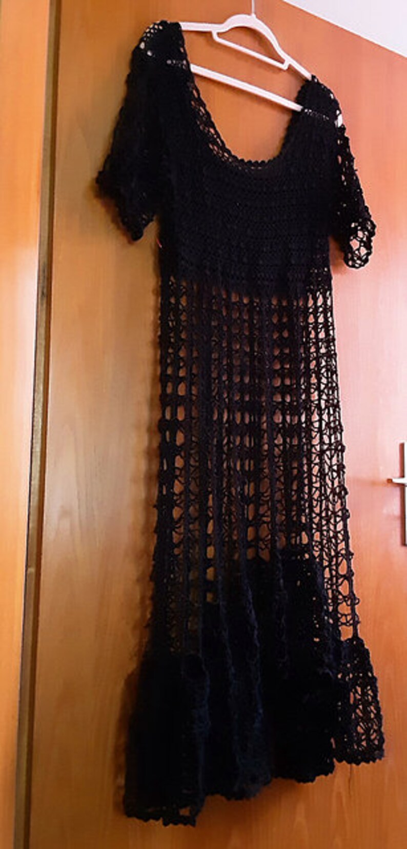 Puede incluir: Un vestido maxi de crochet negro con cuello redondo y mangas cortas. El vestido est&aacute; hecho de una tela ligera y aireada y tiene una silueta fluida.