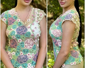 May include: A crocheted top with a floral design in shades of pink, green, and white. The top has a V-neck and short sleeves.