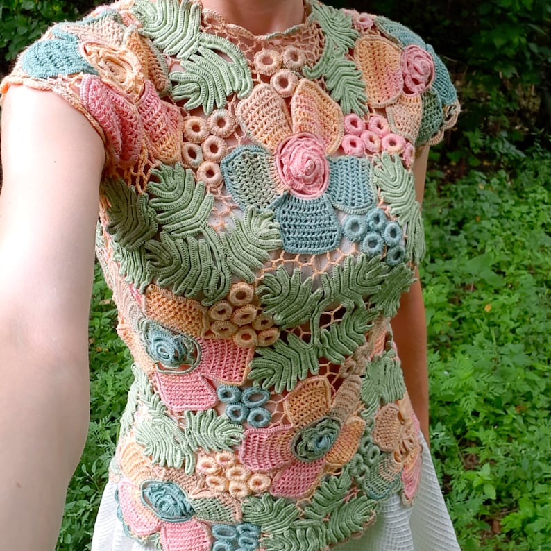 May include: A crocheted top with a floral design in shades of pink, green, and beige. The top is made of delicate crochet stitches and features a variety of floral motifs.