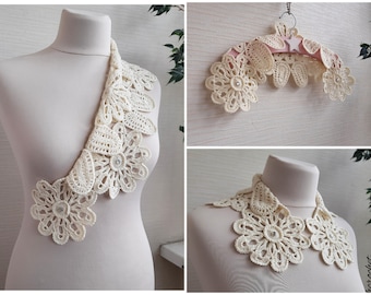 May include: A white crocheted collar with a delicate floral design. The collar is shown on a white mannequin and on a hanger. The collar is made with a fine thread and has a delicate, feminine look.