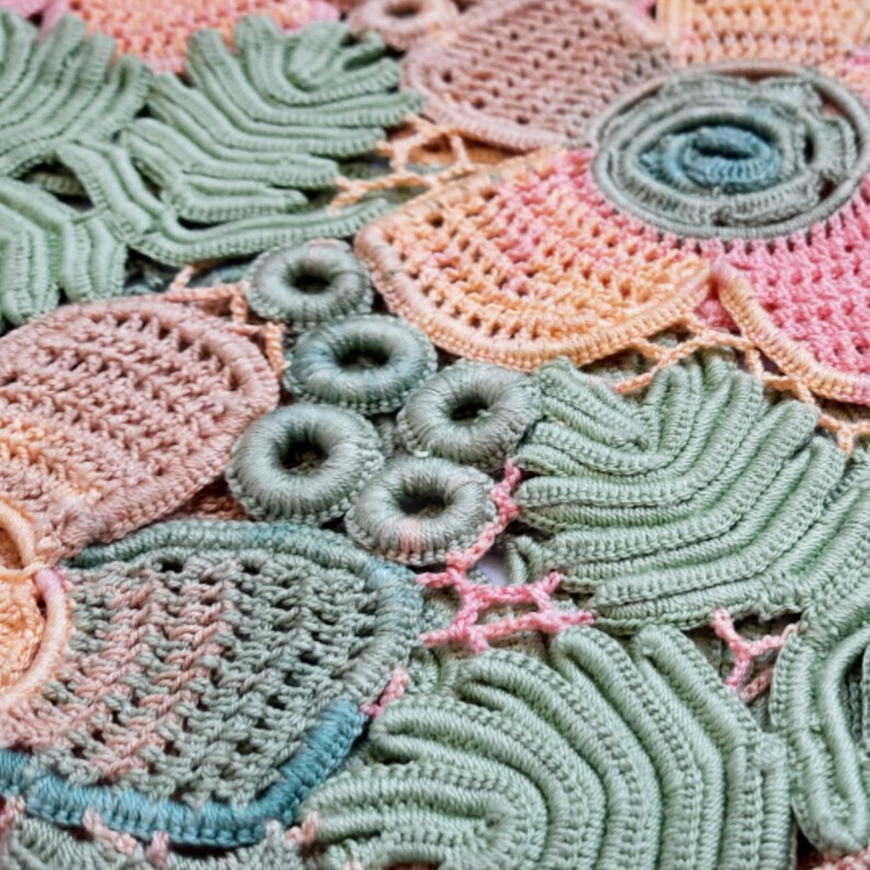 May include: Close-up of a crocheted doily with a variety of pastel colors, including pink, green, and blue. The doily is made up of several different patterns, including circles, flowers, and leaves.