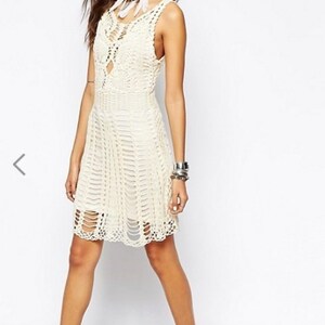 May include: A white crochet dress with a loose fit and a scalloped hem. The dress has a V-neckline and a crochet pattern throughout.