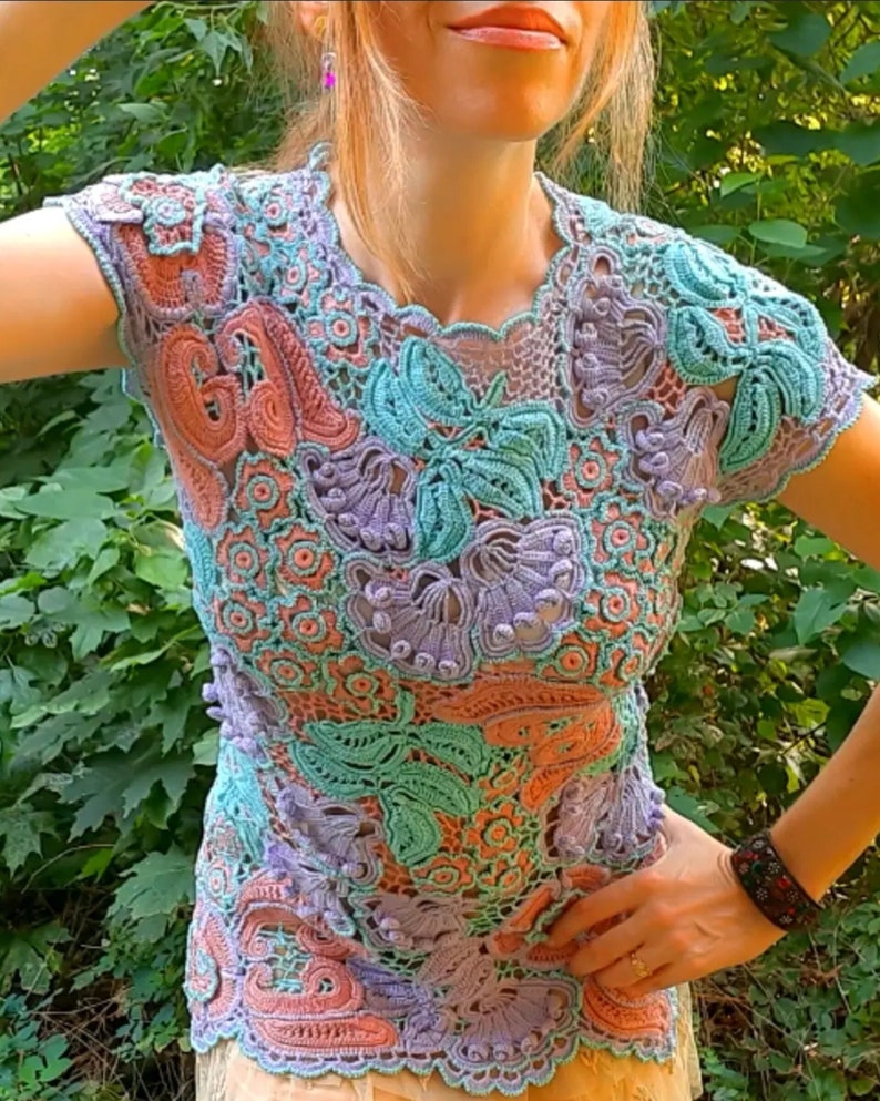 May include: A crocheted top with a floral design in shades of pink, purple, and teal. The top has a round neckline and short sleeves.