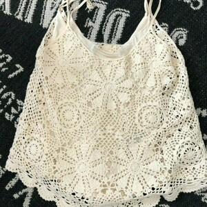 May include: A white crochet tank top with a delicate floral pattern. The top has thin straps and a scalloped hem.