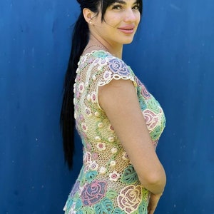 May include: A crocheted top with a floral design in shades of pink, green, and white. The top has a scoop neck and short sleeves.