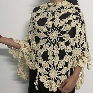 May include: A cream-colored crocheted shawl with a delicate floral pattern. The shawl has a scalloped edge and a fringe.