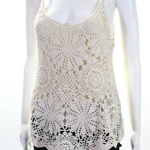 May include: A white crochet tank top with a delicate floral pattern. The top has a scoop neck and thin straps.