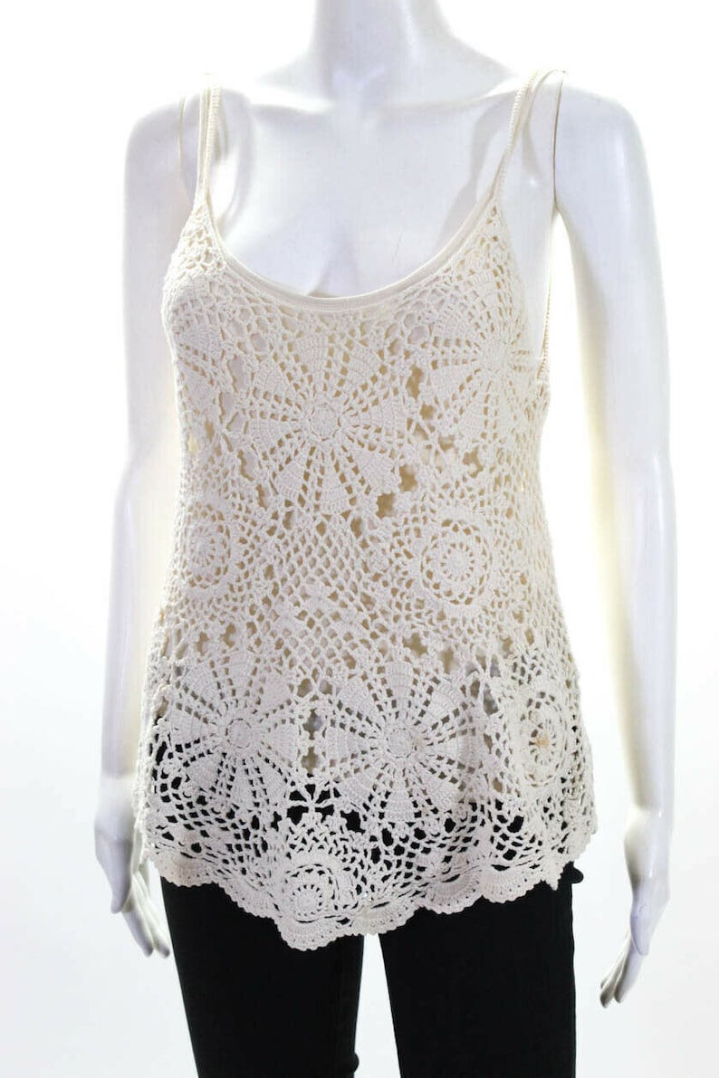 May include: A white crochet tank top with a delicate floral pattern. The top has a scoop neck and thin straps.