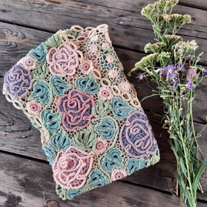 May include: A crocheted shawl with a floral design in shades of pink, green, and blue. The shawl is made with delicate stitches and features intricate roses and leaves.