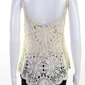 May include: A white crochet tank top with a delicate, intricate pattern. The top has a scoop neck and thin straps.