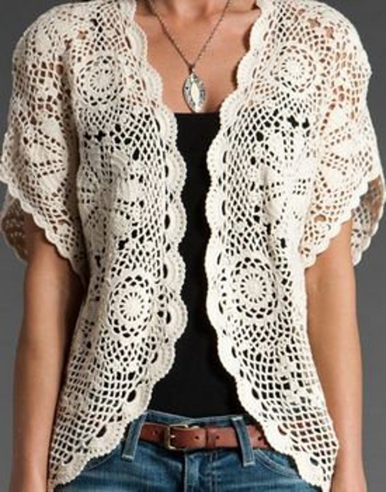 May include: A white crochet cardigan with a delicate floral pattern and short sleeves.
