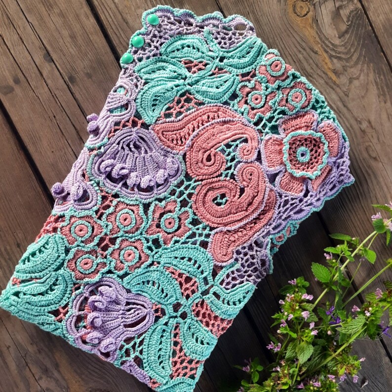 May include: A crocheted lace fabric with a floral design in shades of pink, purple, and teal.