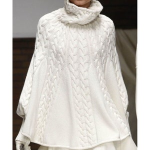 Könnte beinhalten: Weißer Pullover mit Rollkragen und Zopfmuster im Poncho-Stil. Der Pullover hat eine lockere Passform und eine weite, fließende Form.
