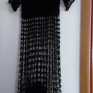 Puede incluir: Un vestido negro de crochet con un corte holgado y un dobladillo festoneado. El vestido est&aacute; hecho de una tela ligera y transpirable y tiene un estilo relajado y bohemio.