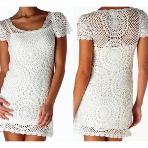 Peut inclure: Une robe blanche au crochet avec une encolure carrée et des manches courtes. La robe présente un motif circulaire détaillé sur le corsage et la jupe. La robe est montrée de face et de dos.