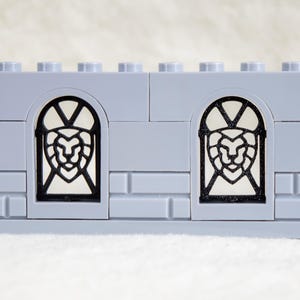 May include: A gray Lego wall with two black windows featuring a lion head design.