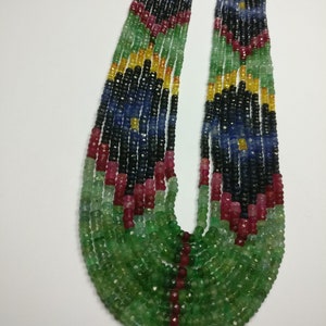 May include: A multi-strand necklace featuring a vibrant array of gemstones. The necklace showcases a gradient of colors, including green, blue, black, red, and yellow beads. The strands are held together with gold-colored clasps, creating a striking and colorful accessory.