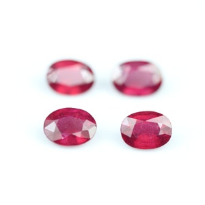 Puede incluir: Cuatro rubíes ovalados y facetados se muestran sobre un fondo blanco. Las piedras preciosas exhiben un tono rojo intenso, con estructuras internas visibles y reflejos de luz. Las gemas están dispuestas en un patrón disperso.