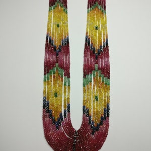 Op de afbeelding: Een ketting met meerdere strengen met een cascade van kleurrijke kralen. De ketting toont een verloop van kleuren, waaronder rood, roze, geel, groen, blauw en zwart. De kralen zijn aan elkaar geregen, waardoor een gelaagde en getextureerde uitstraling ontstaat. De ketting heeft goudkleurige accenten aan de bovenkant.