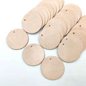May include: A pile of round, light brown leather craft blanks with a hole punched in the centre of each blank.