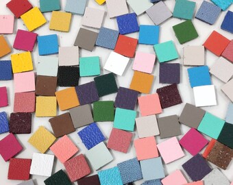 May include: Assortment of small, square leather pieces in various colors, including red, blue, green, yellow, pink, and white. The leather pieces are arranged in a random pattern on a white surface.