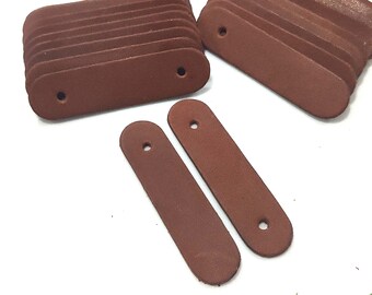 May include: A stack of brown leather strap ends with a hole in the center. Two individual strap ends are also shown.