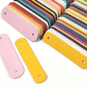 May include: A stack of colorful leather patches, with three individual patches in pink, yellow, and pink. The patches are rectangular and have a hole at each end.