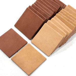 以下が含まれることがあります： 茶色とベージュの革の正方形が積み重ねられています。正方形は2列に並べられており、茶色の正方形が上、ベージュの正方形が下にあります。