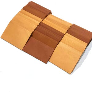 Könnte beinhalten: Ein Stapel Lederquadrate in verschiedenen Brauntönen, von hellem Beige bis Dunkelbraun. Die Lederquadrate sind versetzt angeordnet und bilden so eine visuelle Darstellung der verschiedenen Farben.