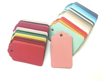 May include: A stack of colorful leather gift tags with scalloped edges and a hole for string. The tags are arranged in a rainbow pattern, with the top tag being a light blue and the bottom tag being a dark red.