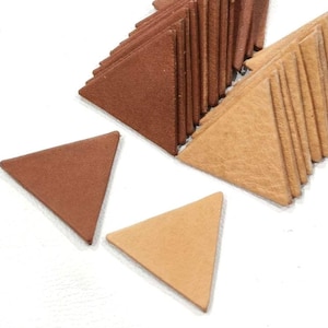 May include: A pile of brown and tan leather triangle shapes. The triangles are stacked on top of each other and are arranged in a pattern. There are two individual triangles at the bottom of the image.