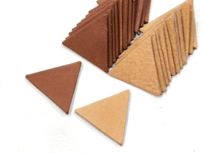 May include: A pile of brown and tan leather triangle shapes. The triangles are stacked on top of each other and are arranged in a pattern. There are two individual triangles in the bottom of the image.