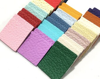 May include: A collection of small, square leather swatches in various colors, including pink, red, teal, blue, and green. The leather has a textured surface, and the swatches are arranged in a diagonal pattern, showcasing the range of hues.