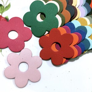 以下が含まれることがあります： 中央に穴が開いたカラフルな革の花の形の詰め合わせ。花は赤、緑、青、黄、茶色の様々な色合いです。