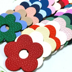 May include: Assortment of colourful leather flower shapes with a hole in the centre. The flowers are arranged in a row, with the red flower in the foreground.