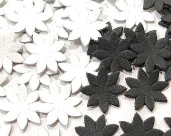 May include: A close-up image of a pile of white and black felt flower embellishments. The flowers have five points and are scattered on a white surface.